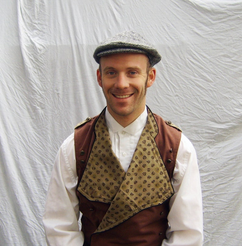May include: A person wearing a tweed newsboy cap, a brown vest with decorative buttons, and a white collared shirt. The vest has a patterned front panel with a brown border. The person is smiling.