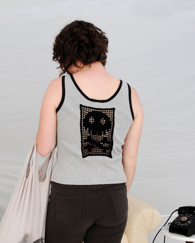 以下が含まれることがあります： 背中が黒のクロシェの骸骨のデザインのグレーのタンクトップ