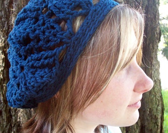 May include: A blue crocheted beanie with a lacy design. The beanie is worn by a person with long, blonde hair.