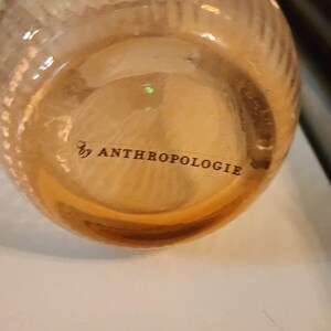 Puede incluir: Una botella de vidrio transparente con una superficie texturizada y el texto "by ANTHROPOLOGIE" impreso en la parte inferior.
