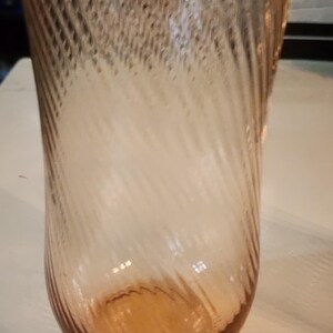 Puede incluir: Un vaso de vidrio transparente con un patr&oacute;n de espiral, el vaso tiene un tono rosa claro.