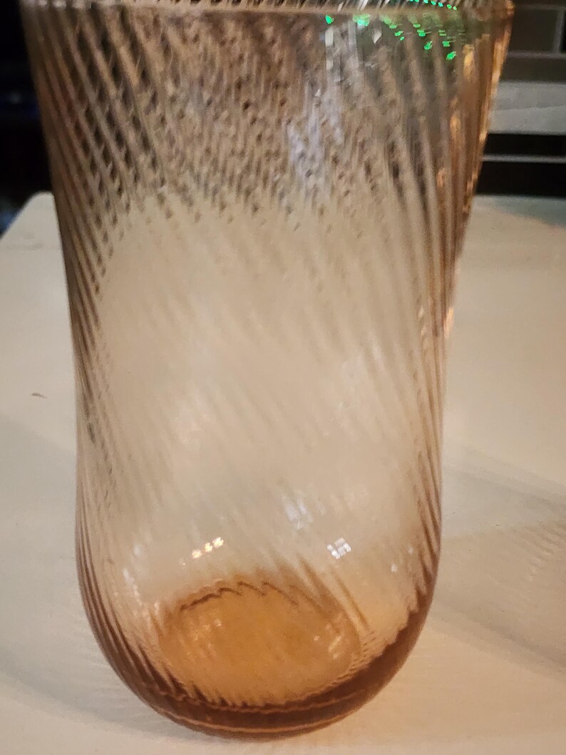Puede incluir: Un vaso de vidrio transparente con un patr&oacute;n de espiral, el vaso tiene un tono rosa claro.