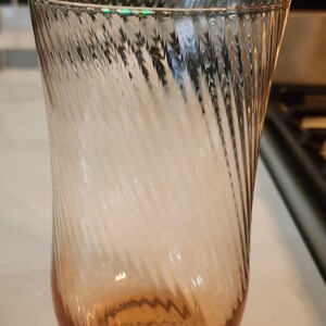 Puede incluir: Un vaso de vidrio transparente con un patr&oacute;n de espiral, la parte inferior del vaso es de color rosa claro.