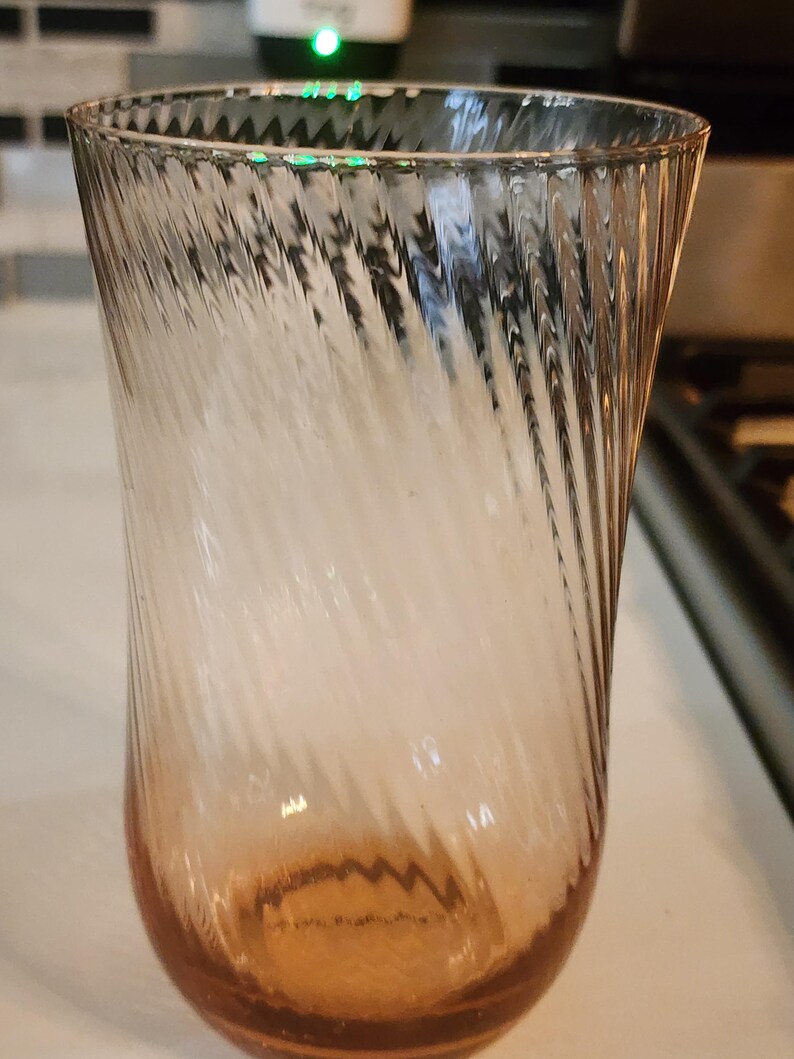 Puede incluir: Un vaso de vidrio transparente con un patr&oacute;n de espiral, la parte inferior del vaso es de color rosa claro.