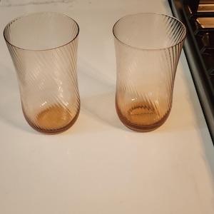 Puede incluir: Dos vasos de beber de vidrio transparente con un dise&ntilde;o de espiral. Los vasos tienen un color &aacute;mbar claro.