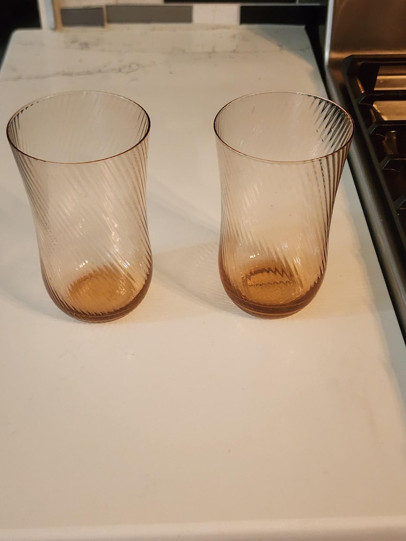 Puede incluir: Dos vasos de beber de vidrio transparente con un dise&ntilde;o de espiral. Los vasos tienen un color &aacute;mbar claro.