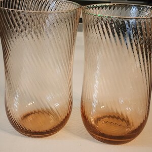 Puede incluir: Dos vasos transparentes de vidrio con un dise&ntilde;o de espiral. Los vasos tienen un tono rosa claro y est&aacute;n vac&iacute;os.