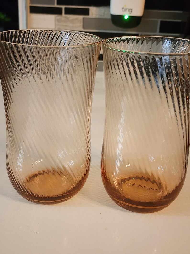 Puede incluir: Dos vasos transparentes de vidrio con un dise&ntilde;o de espiral. Los vasos tienen un tono rosa claro y est&aacute;n vac&iacute;os.