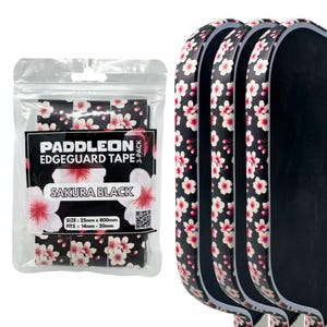 May include: A package of black edge guard tape with a floral sakura design. The package includes three rolls of tape, each with a pattern of pink and white flowers. The text "PADDLEON EDGEGUARD TAPE" and "SAKURA BLACK" are visible on the package.
