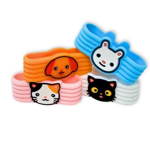May include: Four silicone wristbands featuring animal faces. One is light blue with a white rabbit, one orange with a brown dog, one pink with a calico cat, and one white with a black cat. Each band has a ribbed texture and a flat animal character.