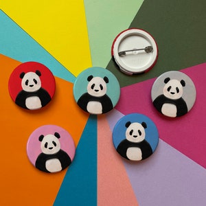 May include: Six round button badges featuring black and white panda bears on different coloured backgrounds. The colours are red, blue, light blue, grey, and green.