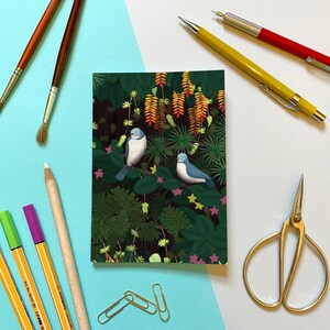 Peut inclure: Une carte avec une illustration colorée de deux oiseaux bleus perchés sur des branches dans un décor de jungle verdoyant et luxuriant. Les oiseaux sont entourés de fleurs orange et jaunes vibrantes.