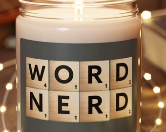 Könnte beinhalten: Eine weiße Kerze mit einem grauen Etikett, auf dem "WORD NERD" in Scrabble-Steinen steht. Die Kerze steht auf einem Holz-Untersetzer und ist von weißen Lichterketten umgeben.