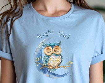May include: A light blue t-shirt featuring a graphic of a blue owl sleeping on a crescent moon. The text "Night Owl" is printed above the owl.