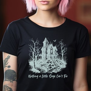 May include: Black t-shirt with a white graphic of a spooky house with trees and a bat. The text "Nothing a Little Sage Can't Fix" is printed below the graphic.