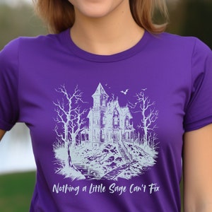 May include: Purple t-shirt with a white graphic of a spooky house with trees and the text "Nothing a little Sage can't fix."