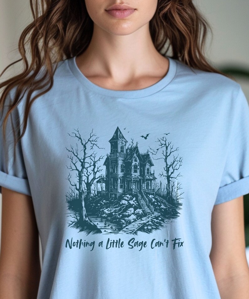 May include: Light blue t-shirt with a graphic of a spooky house in a forest with the text "Nothing a little Sage can't fix".