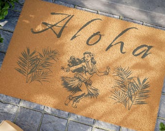 May include: A brown coir doormat with the word "Aloha" in a stylized font and a black and white illustration of a hula dancer with palm leaves on either side.