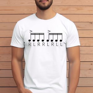 May include: White t-shirt with a black musical notation design for a drum rudiment. The design includes eighth notes and the letters "RLRRLL" below. The shirt is made of a soft, comfortable material.
