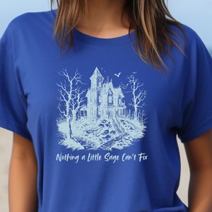 May include: A blue t-shirt with a white graphic of a spooky house and trees. The text "Nothing a little Sage can't fix" is printed below the graphic.