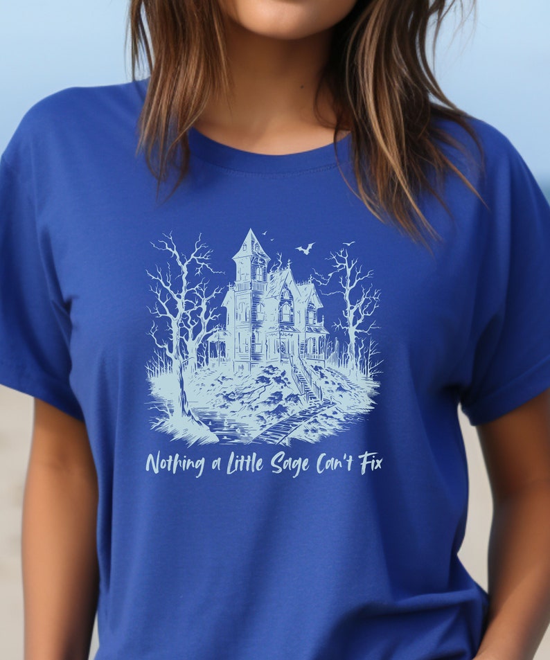 May include: A blue t-shirt with a white graphic of a spooky house and trees. The text "Nothing a little Sage can't fix" is printed below the graphic.