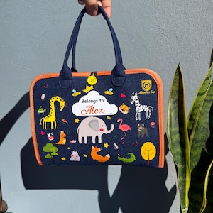 May include: A navy blue tote bag with orange trim and handles. The bag features colorful illustrations of animals, including a giraffe, elephant, and zebra. The text "Belongs to: Alex" is displayed on the front.