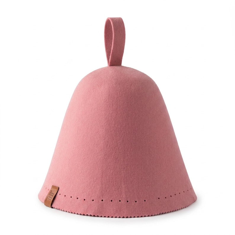 May include: A dusty rose felt sauna hat with a conical shape and a top hanging loop. The base features a decorative row of small perforations and a small brown rectangular leather tag attached to the side with embossed text on the surface.