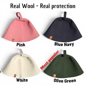 May include: Four felted wool sauna hats with hanging loops, labelled Pink, Blue Navy, White, and Olive Green. The text Real Wool - Real protection appears at the top, and the text Most popular is next to the olive green hat. Each hat has a small tag.