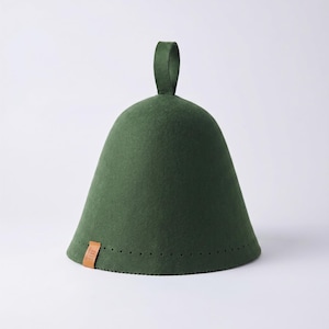 May include: A dark green felt sauna hat with a bell-shaped silhouette and a vertical loop handle at the top. The base features a row of small perforations and a small, rectangular tan leather tag attached to the lower edge of the hat.
