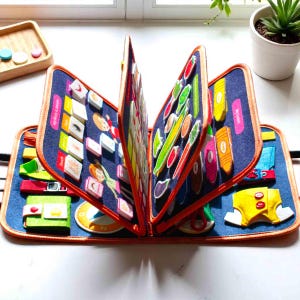 May include: A blue fabric activity book with orange trim, open to display various felt shapes and images. The book features colorful illustrations of food, clothing, and other objects, designed for educational play. The book is designed for children.