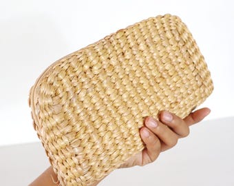 Könnte beinhalten: Eine geflochtene Strohtasche mit Reißverschluss. Die Tasche ist hellbraun und hat einen natürlichen, rustikalen Look.