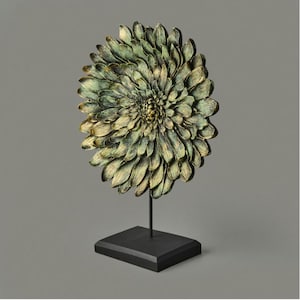 May include: A decorative floral sculpture with a layered petal design, featuring shades of green and gold. The sculpture is mounted on a black metal stand with a square base, creating a striking contrast. This piece is ideal for home decor.