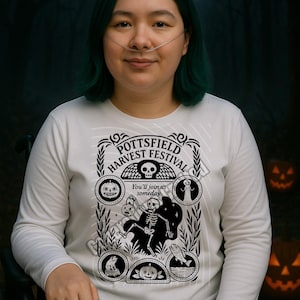 Puede incluir: Camiseta blanca de manga larga con un diseño gráfico en blanco y negro que presenta un esqueleto, calabazas y el texto "Pottsfield Harvest Festival". La camiseta tiene cuello redondo y está hecha de un material suave. También tiene el texto "You'll join us someday".