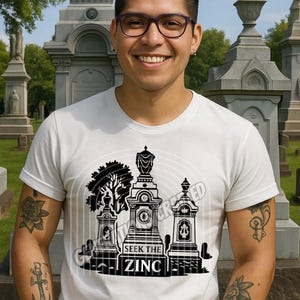 May include: White t-shirt with a black graphic of tombstones and the text "SEEK THE ZINC". The shirt is worn by a person with tattoos and glasses, in a cemetery setting. The words "GENERATIONS CRAFTED" are at the bottom.