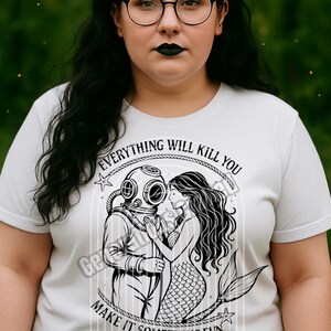 May include: White t-shirt with a graphic of a diver and a mermaid, with the text "EVERYTHING WILL KILL YOU MAKE IT SOMETHING FUN." The shirt has a crew neck and short sleeves. The brand name "Generations Crafted" is at the bottom.