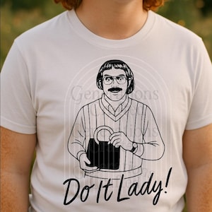 Könnte beinhalten: Hellgraues T-Shirt mit einer Schwarz-Weiß-Illustration eines Mannes mit Brille und Schnurrbart, der eine Handtasche hält. Der Text "Do It Lady!" ist darunter gedruckt.