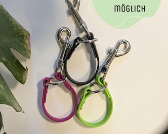 May include: Three silver keychains with different colored silicone loops. The loops are black, purple, and green. The text "Personaliserung möglich" is visible in the background.