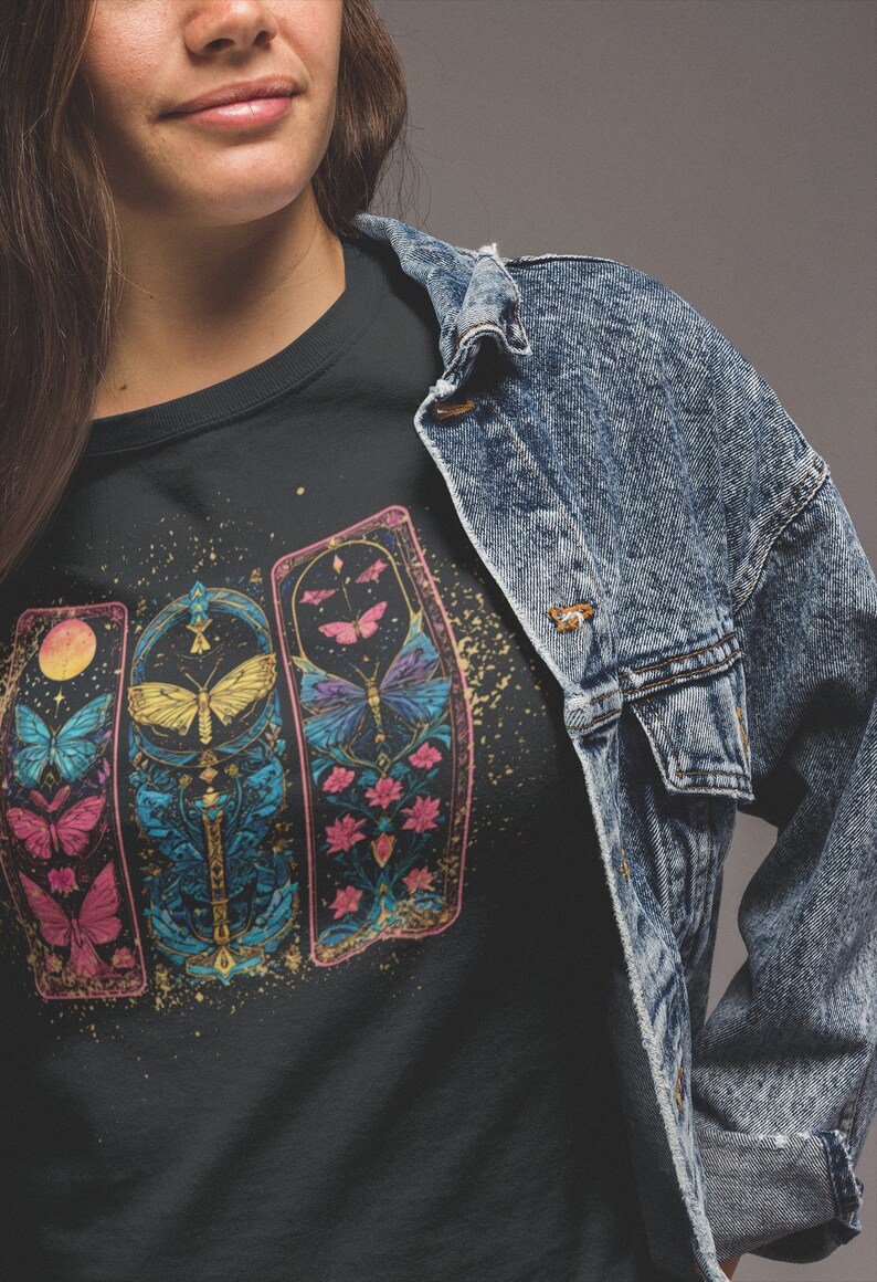 May include: Black t-shirt featuring a graphic of three colourful, ornate panels with butterflies and floral designs. The panels are set against a black background with gold glitter.