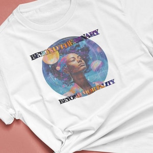 Könnte beinhalten: Weißes T-Shirt mit einem farbenfrohen Grafikdesign, das eine Frau mit Afro-Haaren vor einem Galaxie-Hintergrund zeigt. Der Text "Beyond the Binary" und "Beyond Mortality" ist auf dem Shirt aufgedruckt.