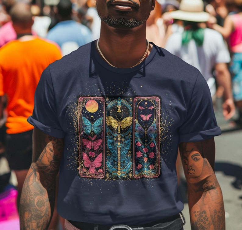 May include: A navy blue t-shirt featuring a graphic print of three vertical panels with butterflies, stars, and floral designs. Each panel has a gold border and a textured background.