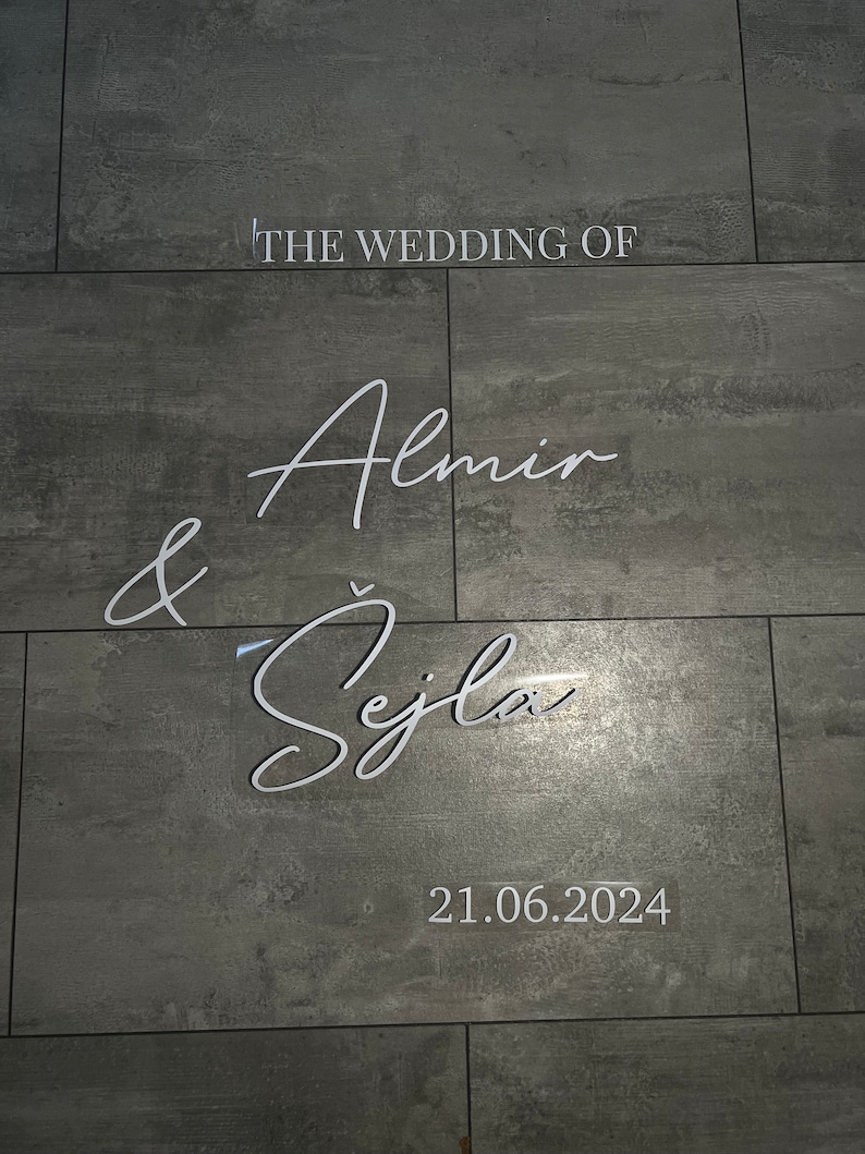 May include: A wedding announcement on a grey tiled wall. The text reads "The Wedding of Almin & &Scaron;ejla 21.06.2024".