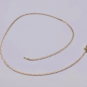 May include: A gold chain necklace with a mariner link design. The chain is lying on a white surface.