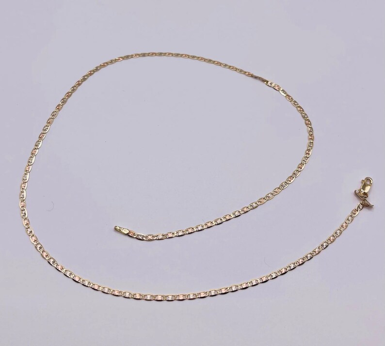 May include: A gold chain necklace with a mariner link design. The chain is lying on a white surface.