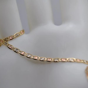 May include: A gold, silver, and rose gold chain bracelet with a delicate, patterned design.