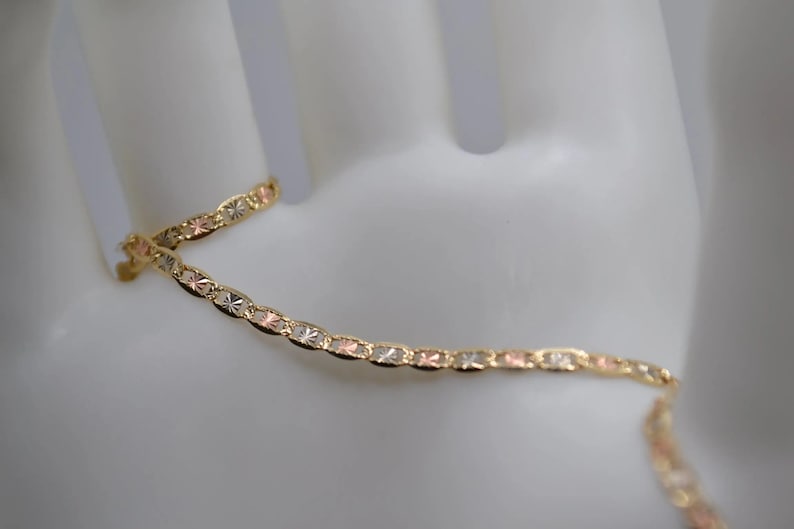 May include: A gold, silver, and rose gold chain bracelet with a delicate, patterned design.