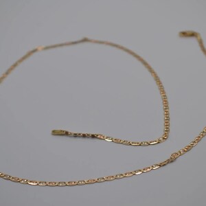 May include: A gold chain necklace with a delicate, linked design. The chain is made of two-toned gold, with a lighter gold color on one side and a darker gold color on the other.
