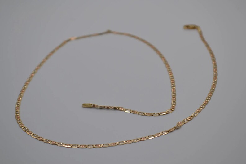 May include: A gold chain necklace with a delicate, linked design. The chain is made of two-toned gold, with a lighter gold color on one side and a darker gold color on the other.