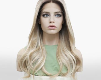 May include: A blonde wig with long, wavy hair. The wig features a dark root and a light blonde ombre effect. The hair is styled with loose waves and falls to the shoulders. The wig is displayed on a mannequin head against a white background.