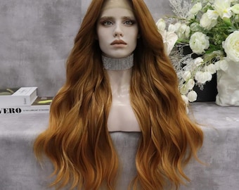 May include: A long, wavy auburn wig with a lace front, styled on a mannequin head. The wig features a natural-looking hairline and a blend of warm, reddish-brown tones. The mannequin wears a silver rhinestone choker. The background includes white flowers.