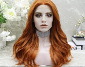 Puede incluir: Peluca larga y ondulada de color rojizo, peinada sobre una cabeza de maniquí. La peluca presenta una línea de cabello natural y un collar de diamantes de imitación brillante. El fondo incluye flores blancas y elementos decorativos.